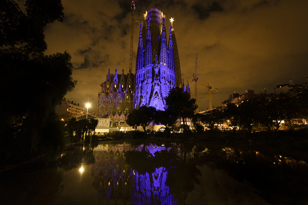 Imatge de la Sagrada Família il·luminada de nit. Davant el monument es troba una font artificial que reflecteix l'estructura.