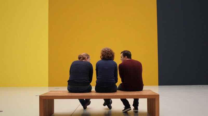 Tres visitants a un museu contemplen una exposició des d'un banc