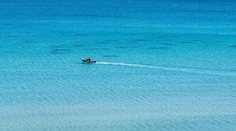 Vista amplia de un mar donde se aprecian distintas tonalidades de azul y en el centro un bote a propulsión desplazando a una persona, dejando una estela blanca a su paso.
